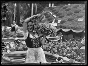 Una ragazza ritratta con un cesto di uva; alle sue spalle numerosi cesti in esposizione