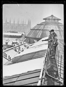 Due uomini sul tetto della Galleria Vittorio Emanuele II, a Milano, spruzzano acqua con un idrante per liberare la copertura dalla neve