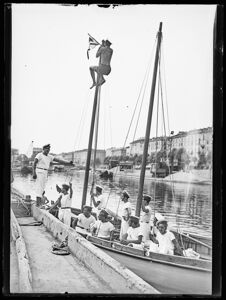 Giovani, in divisa marinara, a bordo di un bialbero con vela latina, attraccato alla Darsena di Porta Ticinese a Milano; uno di loro, arrampicato su un albero, issa una bandiera
