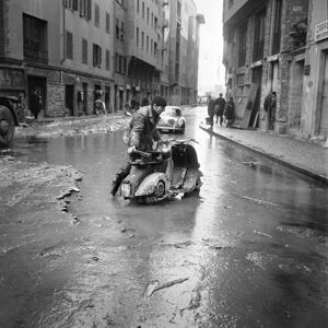 Un uomo spinge una Vespa, con a bordo una bombola di gas, nelle strade di Firenze, invase dal fango, dopo lo straripamento del fiume Arno