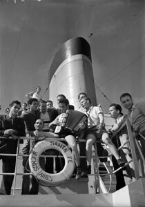 Emigranti italiani, a bordo del piroscafo Santa Fe attraccato nel porto di Genova, in attesa di partire per l'Argentina, suonano la fisarmonica e cantano