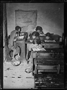 Africo, bambini scalzi seduti ai banchi di scuola; alla parete è affissa la carta geografica della Calabria