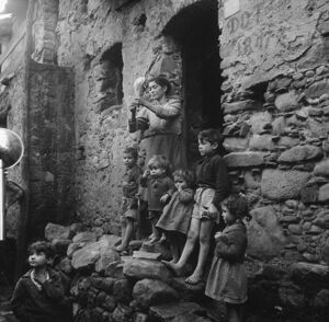 Africo, una donna, con in mano un fuso di filato, sulla soglia di casa ritratta insieme a otto bambini
