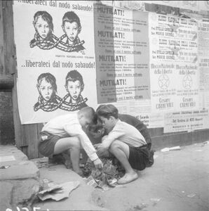 Un gruppo di ragazzini gioca con dei volantini a terra. Sullo sfondo cartelli contro la monarchia sabauda