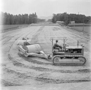 Un uomo al lavoro su un trattore che traina dei rulli compattatori 
					nel cantiere di costruzione dell'Autostrada del Sole, tratta Casalecchio di Reno-Sasso Marconi