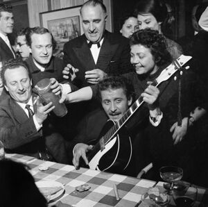 Domenico Modugno, con la chitarra, festeggia con amici, al ristorante, il Festival di Sanremo appena vinto insieme a Johnny Dorelli con la canzone "Piove"