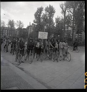 Donne dei Gruppi di difesa della donna (GDD) in bicicletta con bandiere e un cartello che recita: Gruppi di Difesa della Donna