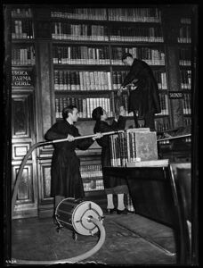 Addetti alla biblioteca puliscono, per mezzo di un'aspirapolvere, i volumi nelle librerie