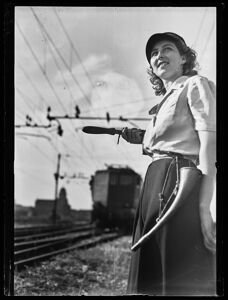 Donna ferroviera ritratta vicino ai binari, sullo sfondo un treno