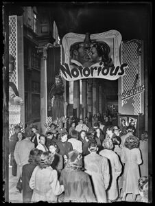 Spettatori accalcati davanti al cinema Odeon di Milano decorato con grandi manifesti pubblicitari del film "Notorious" di Alfred Hitchcock