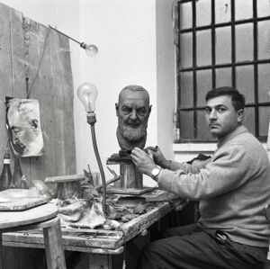Lo scultore Mario Moretto al suo tavolo di lavoro con scultura della testa di Padre Pio