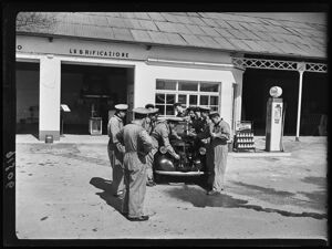 Allievi di un corso per addetti alle stazioni Esso durante un'esercitazione, intorno a un'automobile, in una stazione di servizio