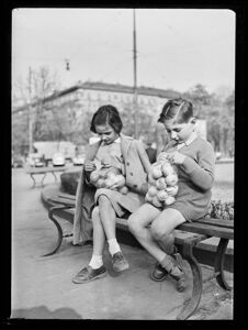 Due bambini, seduti su una panchina, esaminano un sacchetto di cellophane pieno di mele