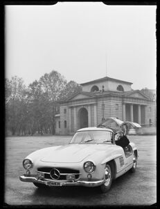 Una donna fa capolino dietro la portiera, con apertura a ali di gabbiano, di una Mercedes 300 SL in piazza Sempione