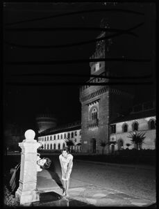 Veduta notturna del Castello Sforzesco di Milano. In primo piano due donne bevono a una fontanella