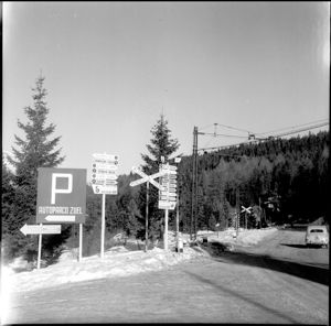 Nei cartelli le indicazioni per le varie sedi delle competizioni olimpiche, per i parcheggi e per il Centro stampa. A destra una Fiat 1100/103 Industriale.<br>