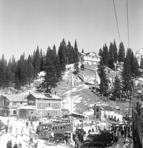 Sullo sfondo la casa cantoniera della strada statale n. 48 delle Dolomiti, sul cui tetto sono accucciate alcune persone per vedere le gare di pattinaggio, sulla cima della collina l'Albergo Bellavista.<br>