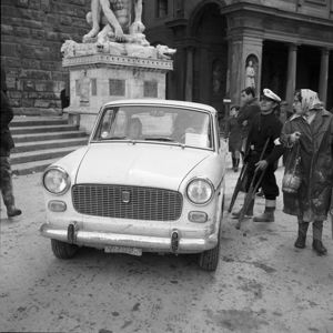 In primo piano una Fiat 1100 con il contrassegno della questura, sullo sfondo a sinistra la scultura di Ercole e Caco e a destra la Galleria degli Uffizi.<br>