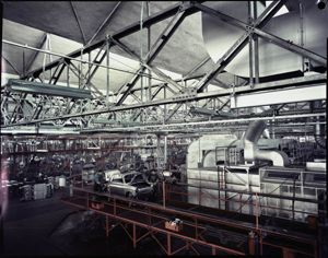 Tre operai lavorano sulla carrozzeria di un'automobile, modello Bianchina<br>