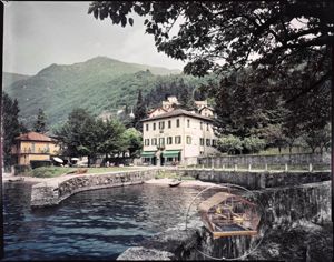 Albergo Plinio con in primo piano una voliera ed il lago. Sullo sfondo le montagne<br>