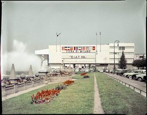 Sulla sinistra è visibile parte della fontana presente nella piazza, mentre sulla facciata dell'edificio è presente la scritta: Fiera di Milano "E.I.A.T 59"<br>