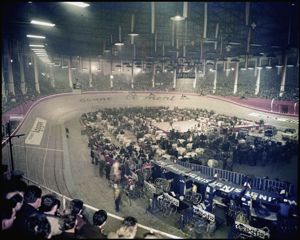 Al centro della pista sono visibili un palco, tavoli con sedie, automobili in esposizione e le postazioni delle squadre in gara. Sono inoltre visibili le seguenti insegne pubblicitarie: gomme Clement, Agipgas, Ignis, Zucca<br>